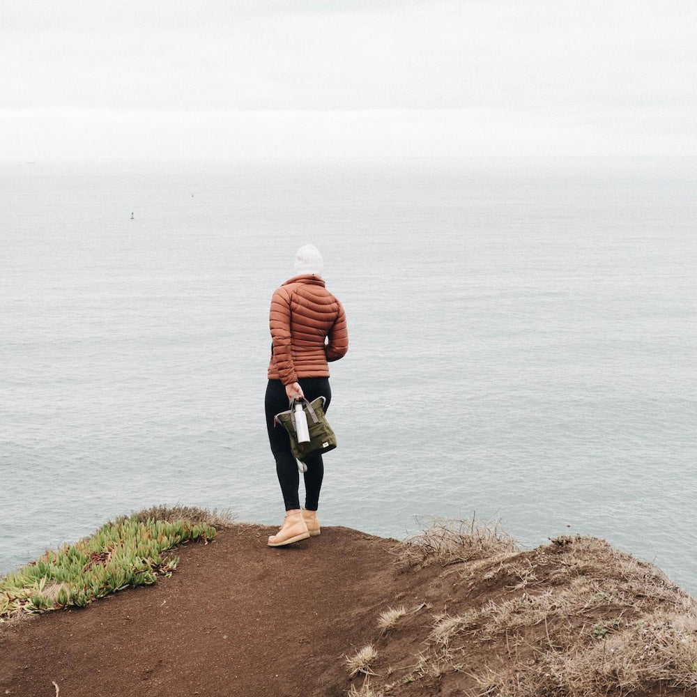 Woman looking out to ocean with Ori Backpack in hands.